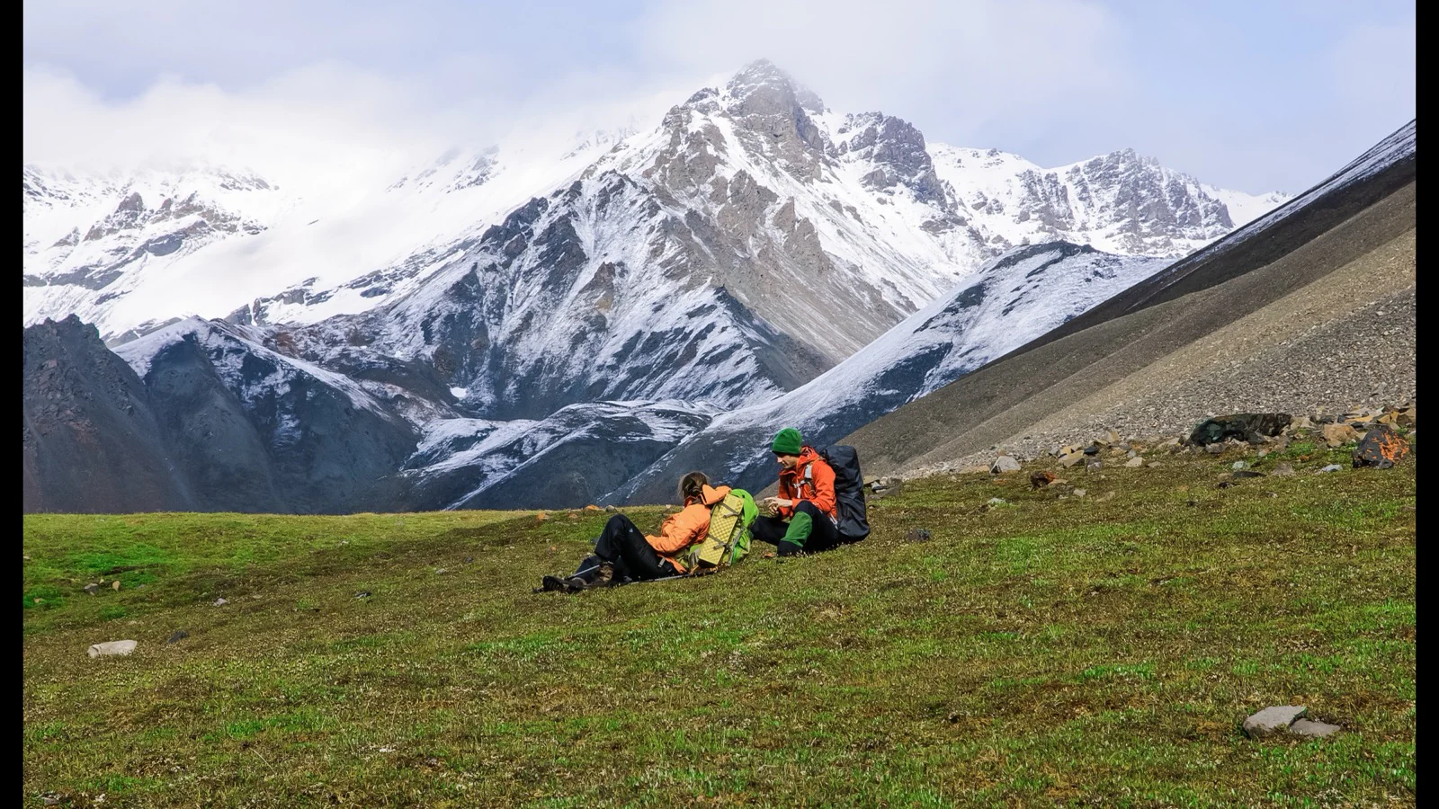 Two backpackers resting in alpine tundra below snow-covered mountains in Wrangell-St. Elias
