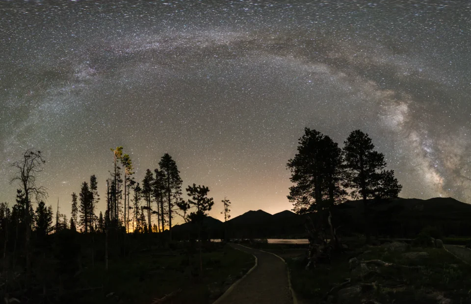 Milky Way arching above silhouetted trees and mountains in Rocky Mountain National Park