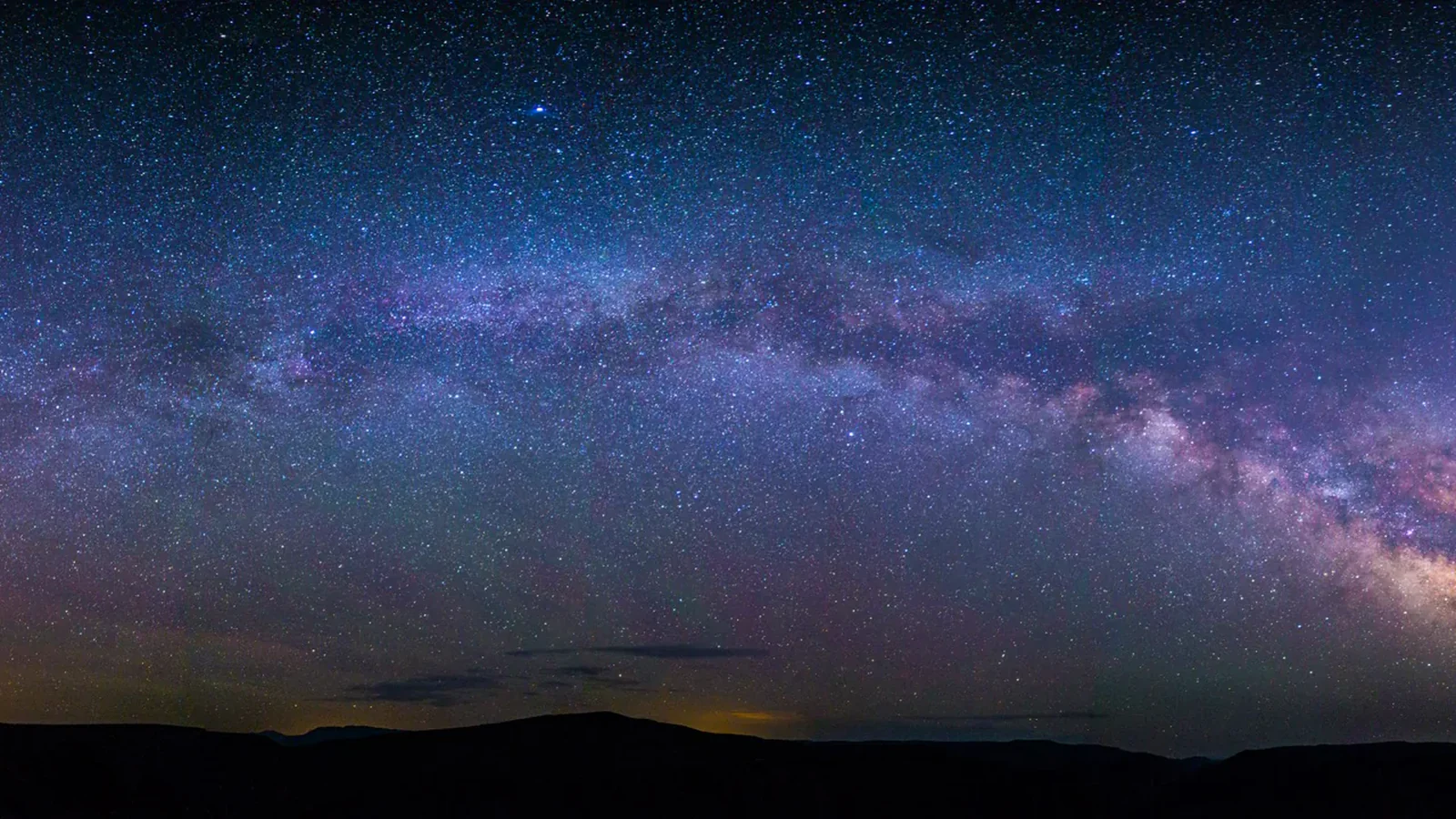 A dense field of stars and the Milky Way above the dark rim of Black Canyon of the Gunnison National Park