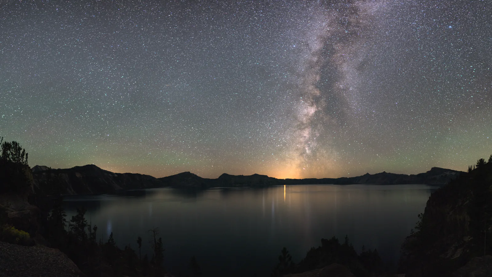 The Milky Way rises above the dark caldera and still water of Crater Lake National Park