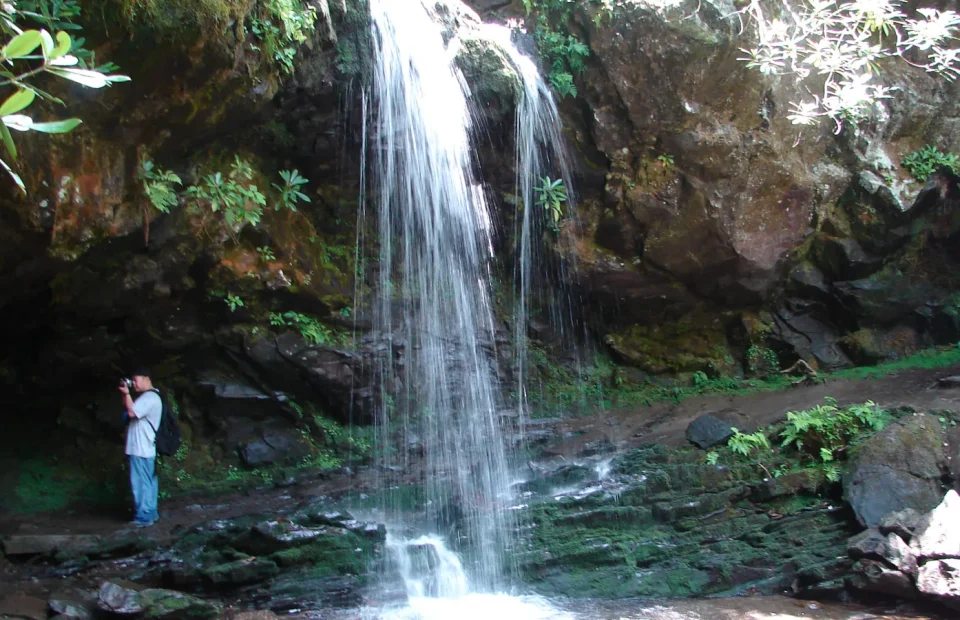 Water falls over a rock ledge beside a hiker on a Great Smoky Mountains National Park trail